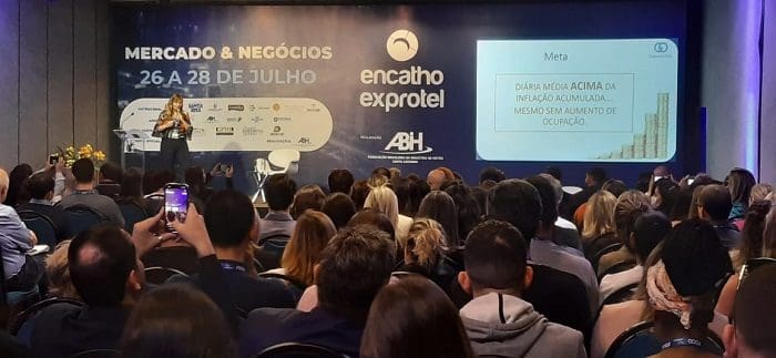 Gabriela Otto, no palco do Encatho & Exprotel 2022, em Florianópolis-SC, explica aos presentes o estudo apresentado no projetor.