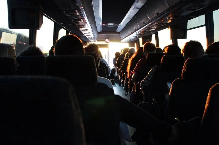 Interior de um ônibus de viagem, com várias pessoas sentadas e de costas. O sol está batendo e é possível ver a silhueta delas. Volume de viagens de ônibus deve crescer em até 40% no final de ano.