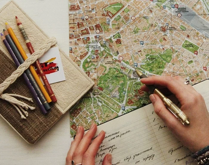 Mão de uma pessoa em cima de um mapa e de um caderno, planejando viagem. Pesquisa mostra que 53% dos brasileiros pretendem viajar em 2023