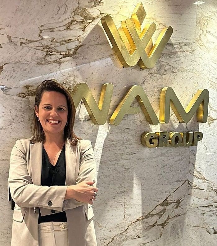 wam_group_anuncia_fernanda_oliveira_como_nova_diretora_de_vendas_de_hotelaria WAM Group anuncia Fernanda Oliveira: imagem da executiva em frente ao logo da empresa em dourado