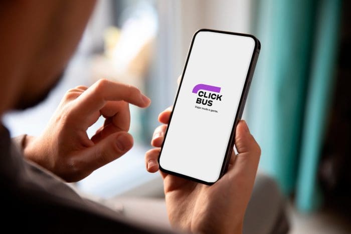 Viagens rodoviárias crescem 49%: pessoa olhando um celular e na tela, aparece o novo logo da ClickBus