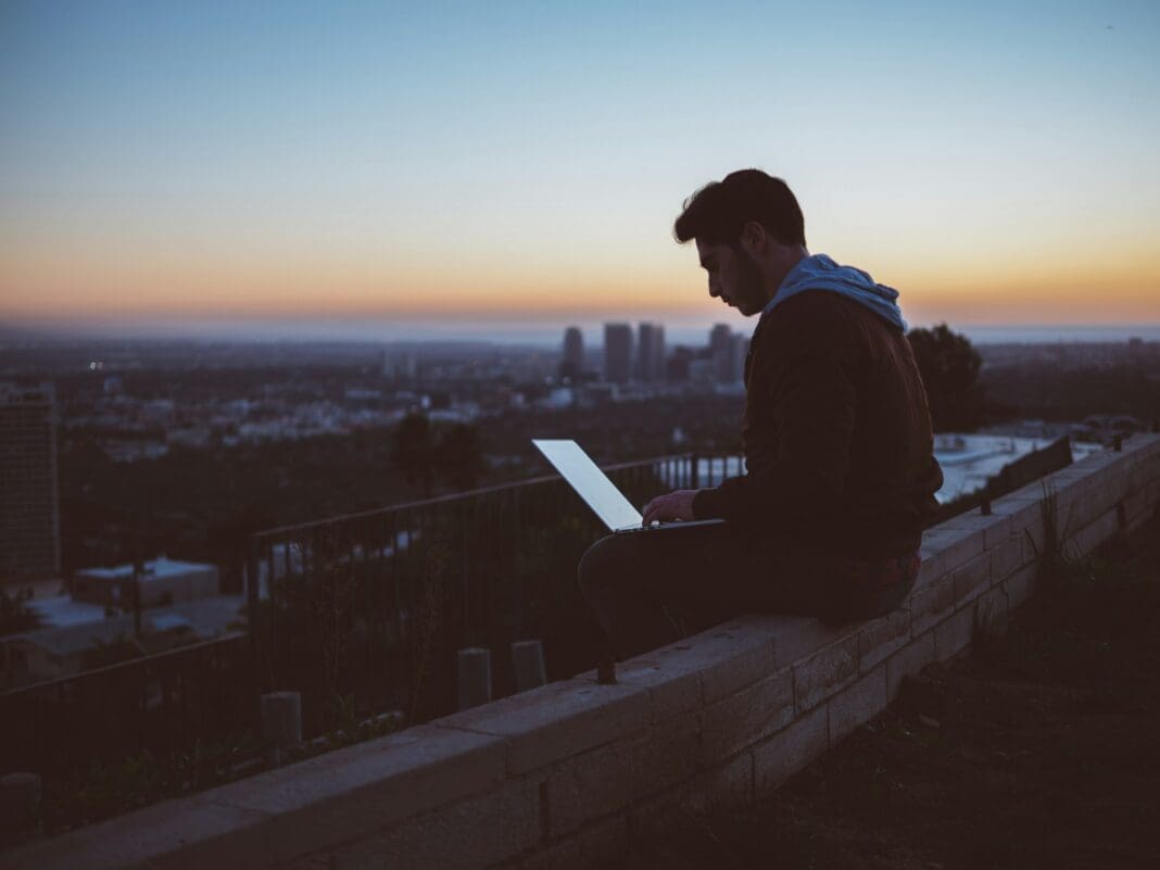 avi-richards-Z3ownETsdNQ-unsplash (2) homem sentado em tijolo de concreto com portátil aberto em seu colo