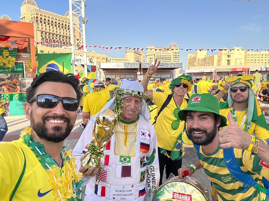 Daniel Sbruzzi (ao centro), recordista mundial de presenças em Copas do Mundo reconhecido pelo Guinness World Records, posa com a réplica da taça ao lado de torcedores brasileiros durante o Mundial. - Crédito: Divulgação / VIRA Assessoria