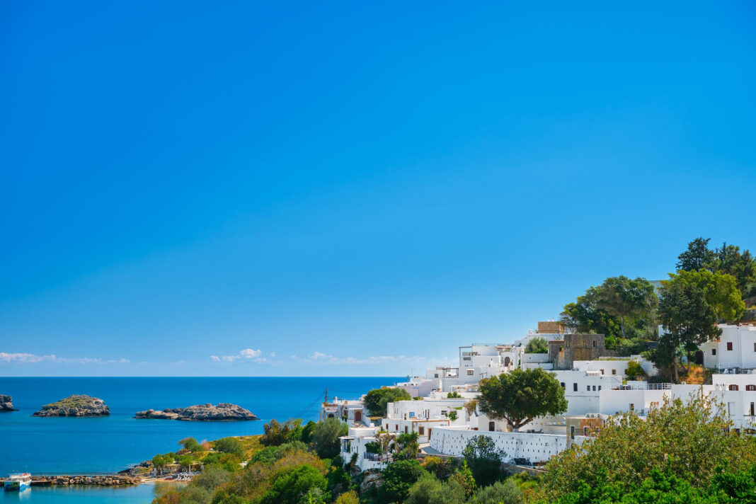 Vista da histórica vila de Lindos, na ilha grega de Rodes, um dos destinos que impulsionam o crescimento da intenção de viagens ao sul da Europa no verão de 2026. Ao fundo, o Mar Egeu completa um dos cenários mais emblemáticos do Mediterrâneo. Crédito: Magnific / Freepik